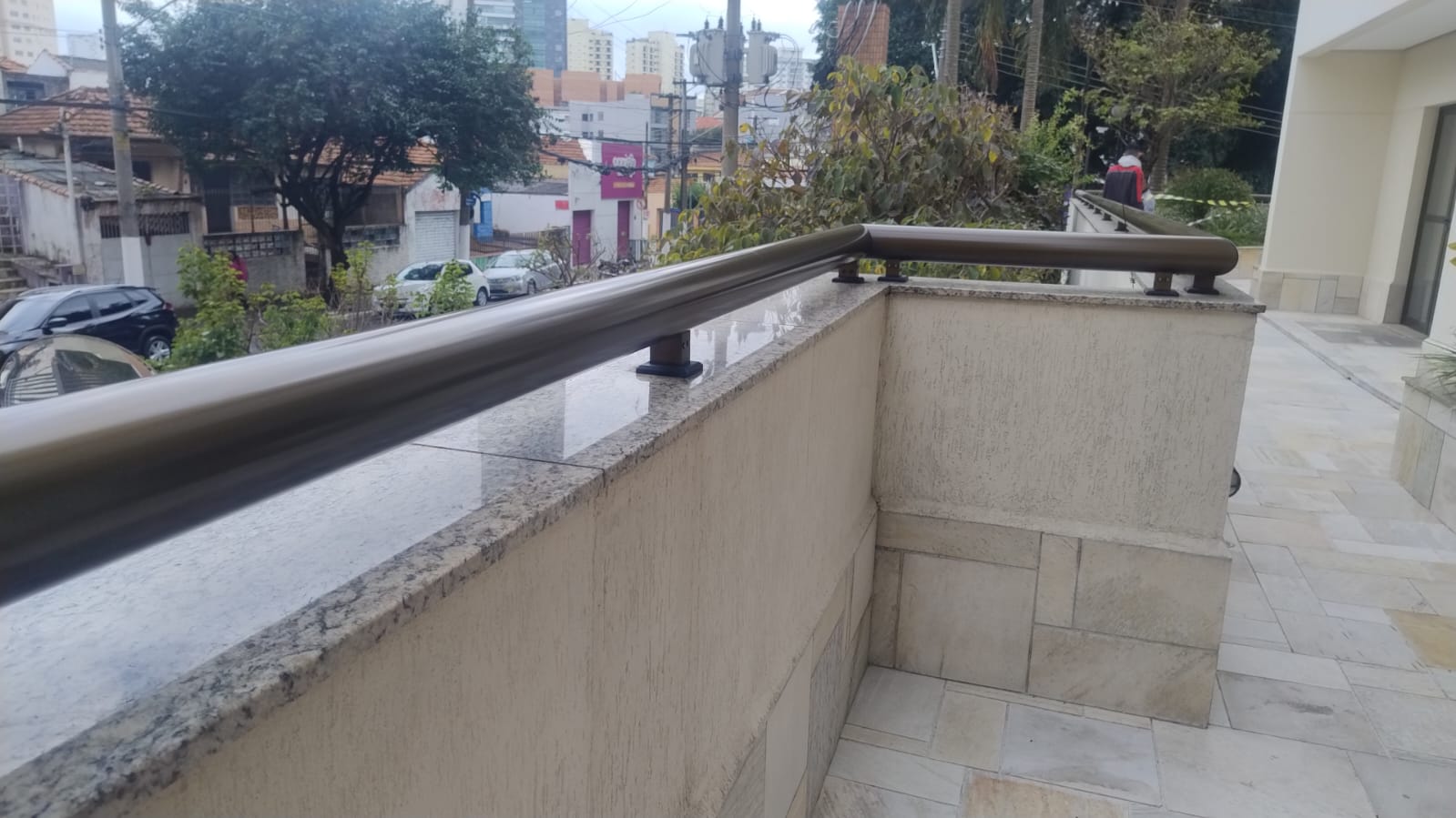 Corrimão tubular metálico com acabamento acetinado fixado sobre mureta de granito